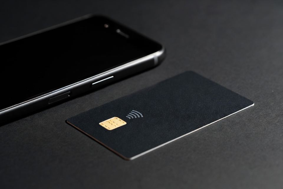 Cartão de pagamento sem número e sem bandeira, ao lado de um celular com a tela virada para baixo.
