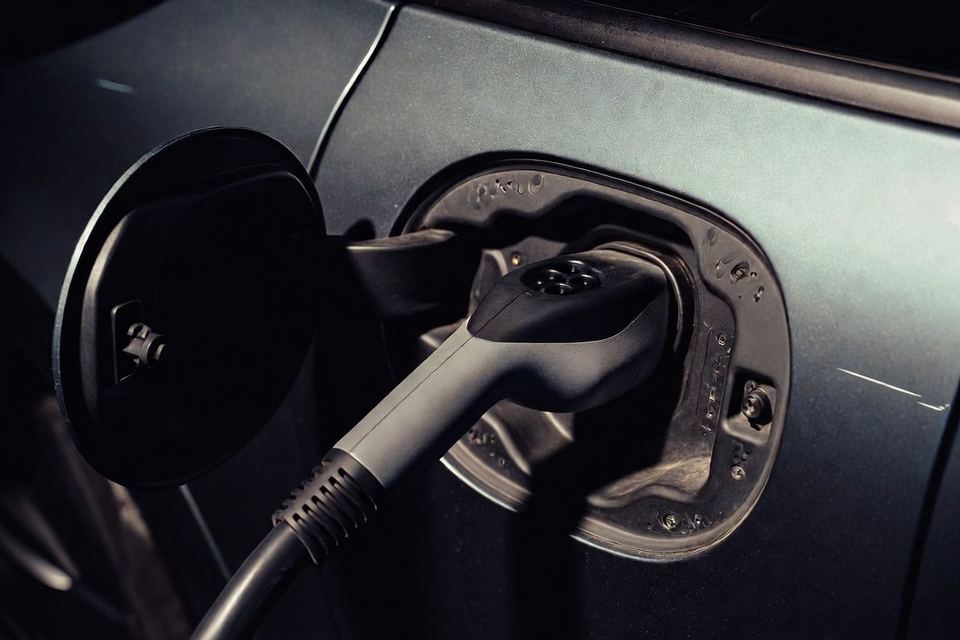 Porta de carga aberta de um carro elétrico, com o conector encaixado.