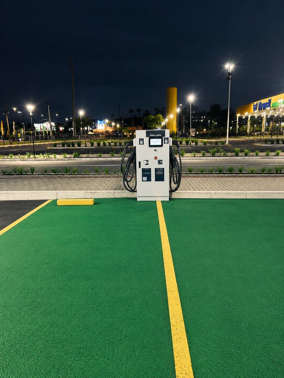 Carregador DC de 80 kW da Elektro Charge na vaga verde do estacionamento do Multi Space Araquari, à noite, com o Brasil Atacadista ao fundo
